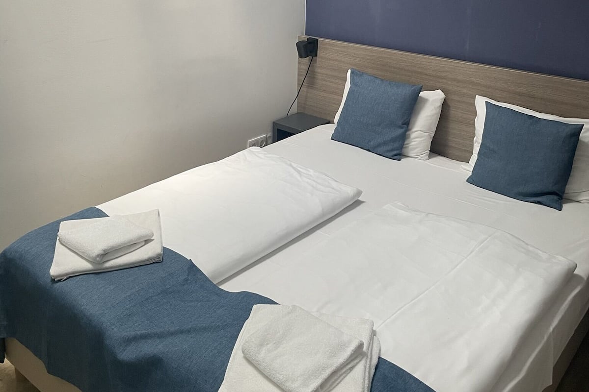 A neatly made bed with white and blue bedding, a wooden headboard, and a nightstand with a lamp.