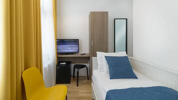 A hotel room with a bed, a desk with a computer, a chair, and a wardrobe.