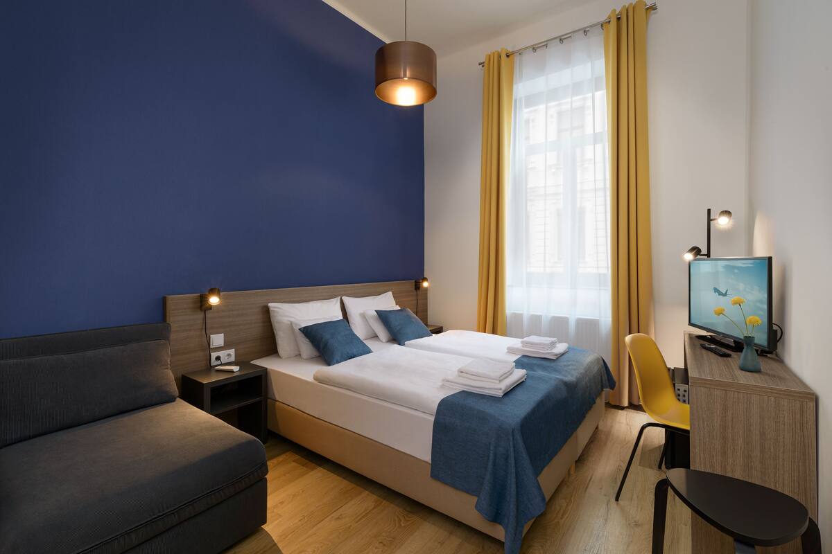 A modern hotel room with a large bed, a sofa, a desk with a computer, and a TV.