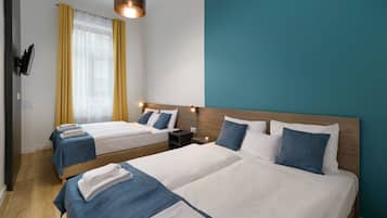 Quarto de hotel com duas camas, uma televisão presa à parede e piso de madeira.