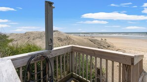 Una terraza de madera con vista a una playa arenosa y cielo despejado.