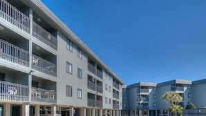 Un edificio residencial de varios pisos con balcones, un estacionamiento y un cielo azul despejado.