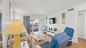 Ein modernes Wohnzimmer mit einer Couch, Sesseln, einem Couchtisch, einem Fernseher und einer Lampe.