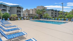 Un espace piscine doté de chaises longues et d’une piscine, le tout entouré d’immeubles à plusieurs étages avec des balcons.