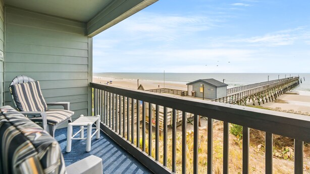 Un balcon avec vue sur la plage et la jetée, comprenant une chaise et une petite table.