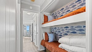 A narrow hallway with a bunk bed, a patterned wall, and a view into another room.
