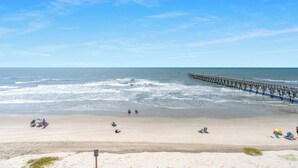 A beach with a pier extending into the water, sandy shore, and a few people relaxing.