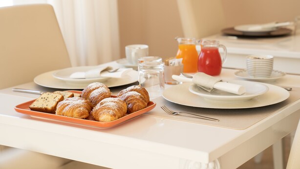 Una mesa de desayuno con pasteles, un jarro de zumo de naranja y una pila de platos.