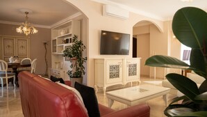 Una sala de estar con un sofá de cuero rojo, una mesita de centro blanca y un televisor montado en la pared.