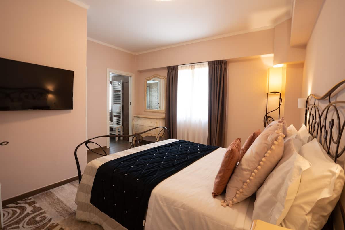 Une chambre d’hôtel avec un lit, un téléviseur fixé au mur, un bureau avec une chaise et une fenêtre avec des rideaux.