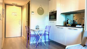 A compact kitchen with modern appliances, a dining table with chairs, and a small seating area. - Maison Linda (Niza)