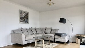 Un salon moderne avec un canapé d’angle gris, une table basse en verre, un lampadaire noir et une œuvre d’art murale aux motifs de marbre.