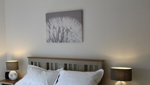 Un lit bien fait, avec du linge de lit blanc, deux tables de chevet avec des lampes et une œuvre d’art accrochée au mur.