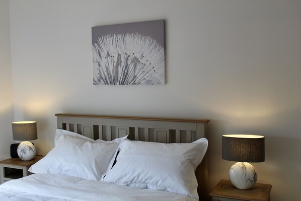 Un lit bien fait, avec du linge de lit blanc, deux tables de chevet avec des lampes et une œuvre d’art accrochée au mur.