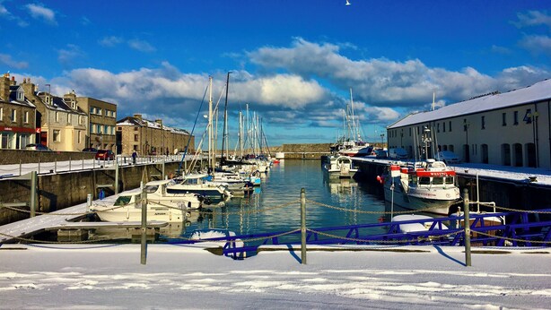 Un port de plaisance avec des bateaux amarrés, un bâtiment avec une enseigne et un ciel dégagé.