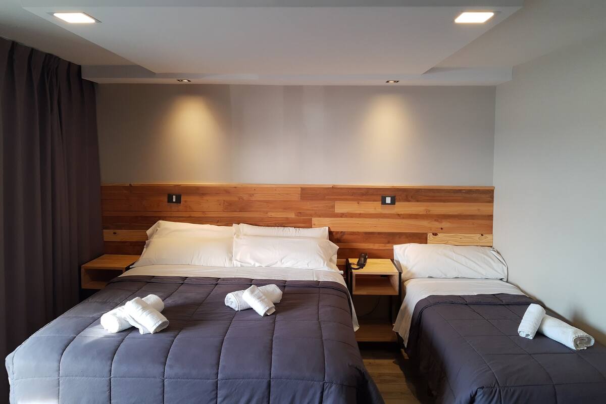 Ein Hotelzimmer mit zwei Betten, jeweils mit einem hölzernen Kopfteil, und einem Nachttisch dazwischen.