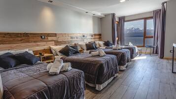Habitación de hotel con cuatro camas dispuestas en fila, un ventanal con vista al mar y un cabecero de madera.