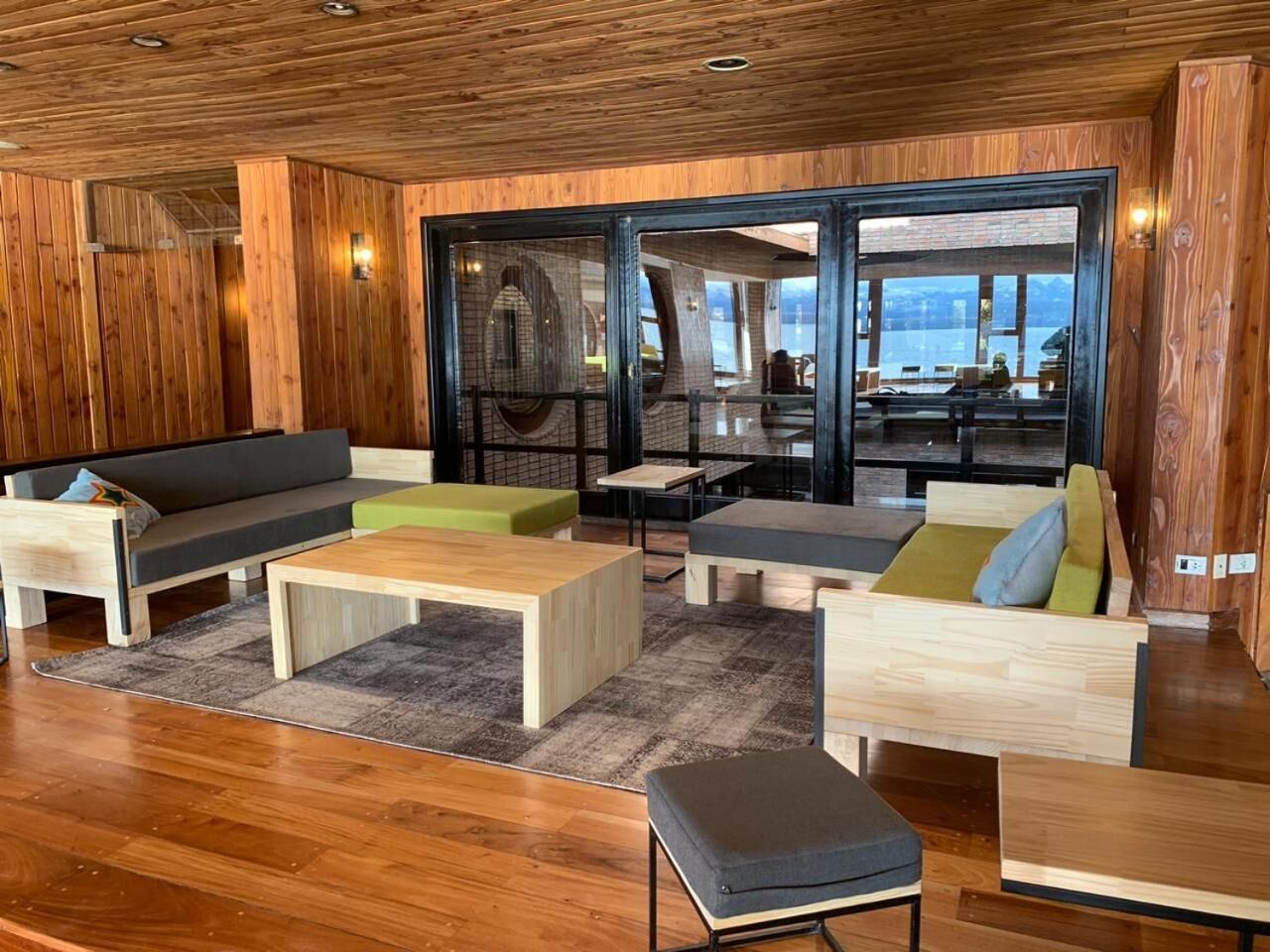 A modern interior with wooden paneling, a central seating area with sofas and a coffee table, and a view of a dining area through glass doors.