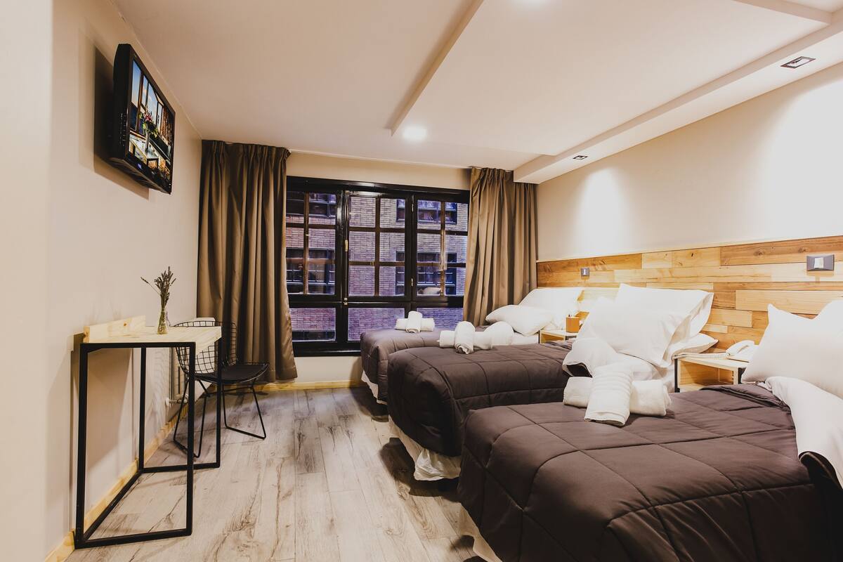 Ein Hotelzimmer mit zwei Betten, einem Schreibtisch, einem Fernseher und einem Vorhangfenster.