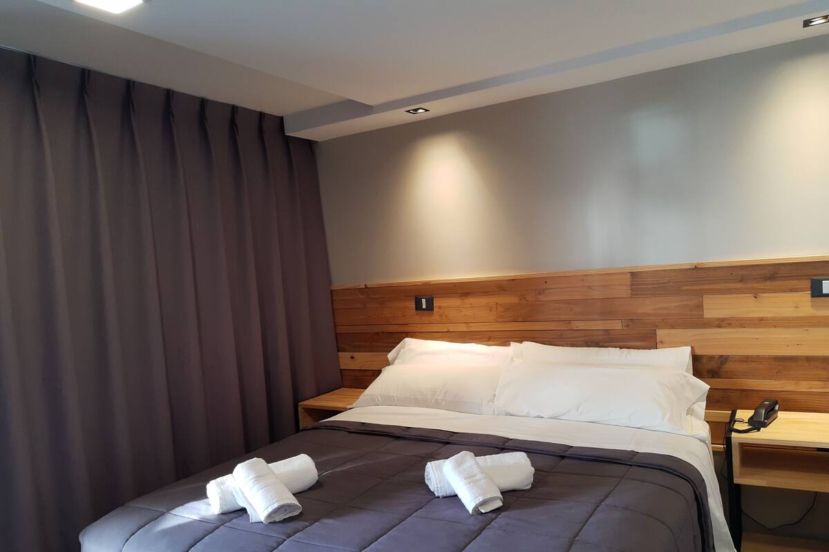 Ein modernes Hotelzimmer mit einem großen Bett, einem Holz-Kopfteil und einem Nachttisch mit Telefon.