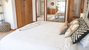 Une chambre à coucher avec un grand lit, des coussins à motifs, une armoire en bois et une porte coulissante en verre donnant sur une autre pièce.