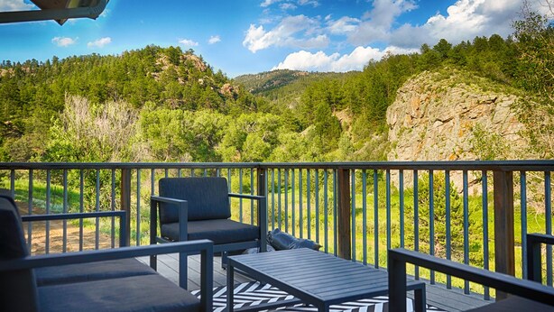 Un balcon agrémenté de mobilier d’extérieur, une vue sur une vallée boisée et un ciel dégagé.