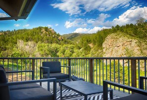 Ein Balkon mit Gartenmöbeln, Blick auf ein bewaldetes Tal und einen klaren Himmel.
