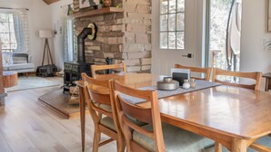 Un coin repas chaleureux avec une table et des chaises en bois, une cheminée en pierre et une vue sur l’extérieur.