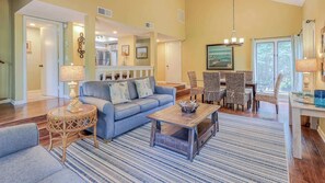 A spacious living room with a blue sofa, a coffee table, and a dining area with wicker chairs.