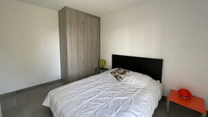 Una camera da letto con un letto grande, una testiera nera, un tavolino con un oggetto rosso e un'armadio alta.