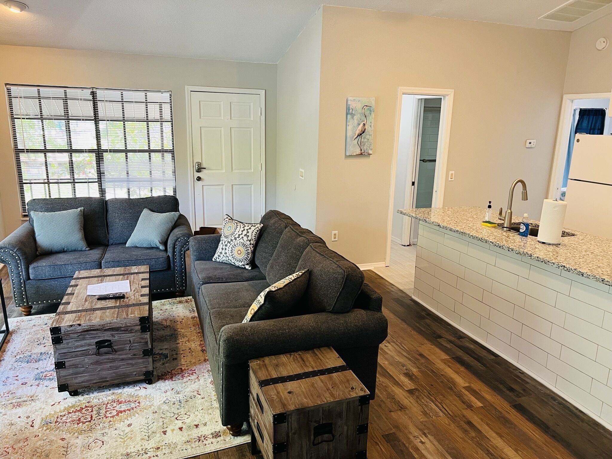 A living room with two sofas, a coffee table, and a rug. There is a kitchen area with a sink and countertop.