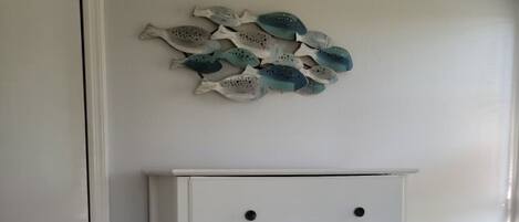 A white dresser with five drawers and black knobs, positioned next to a white door and a wall with a decorative fish art piece.