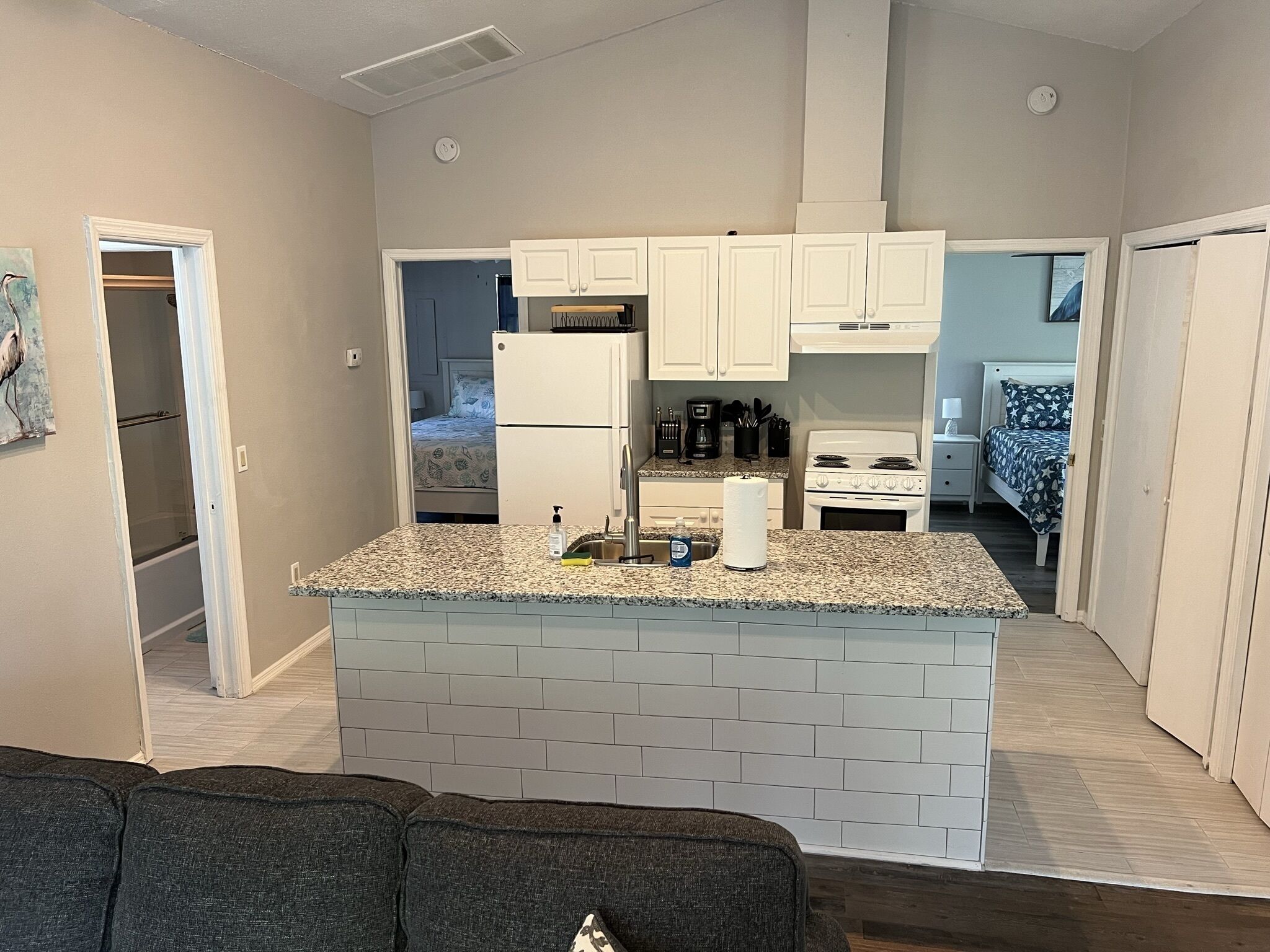 A compact kitchen with white cabinets, a granite countertop, a refrigerator, a stove, and a sink.