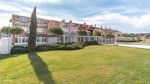 Une rangée d’immeubles résidentiels à plusieurs étages, avec une pelouse bien entretenue et un grand arbre au premier plan.