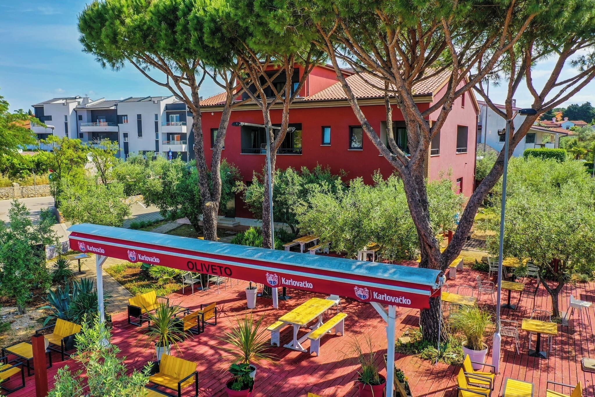 An outdoor seating area with tables and chairs, surrounded by trees and a building in the background.