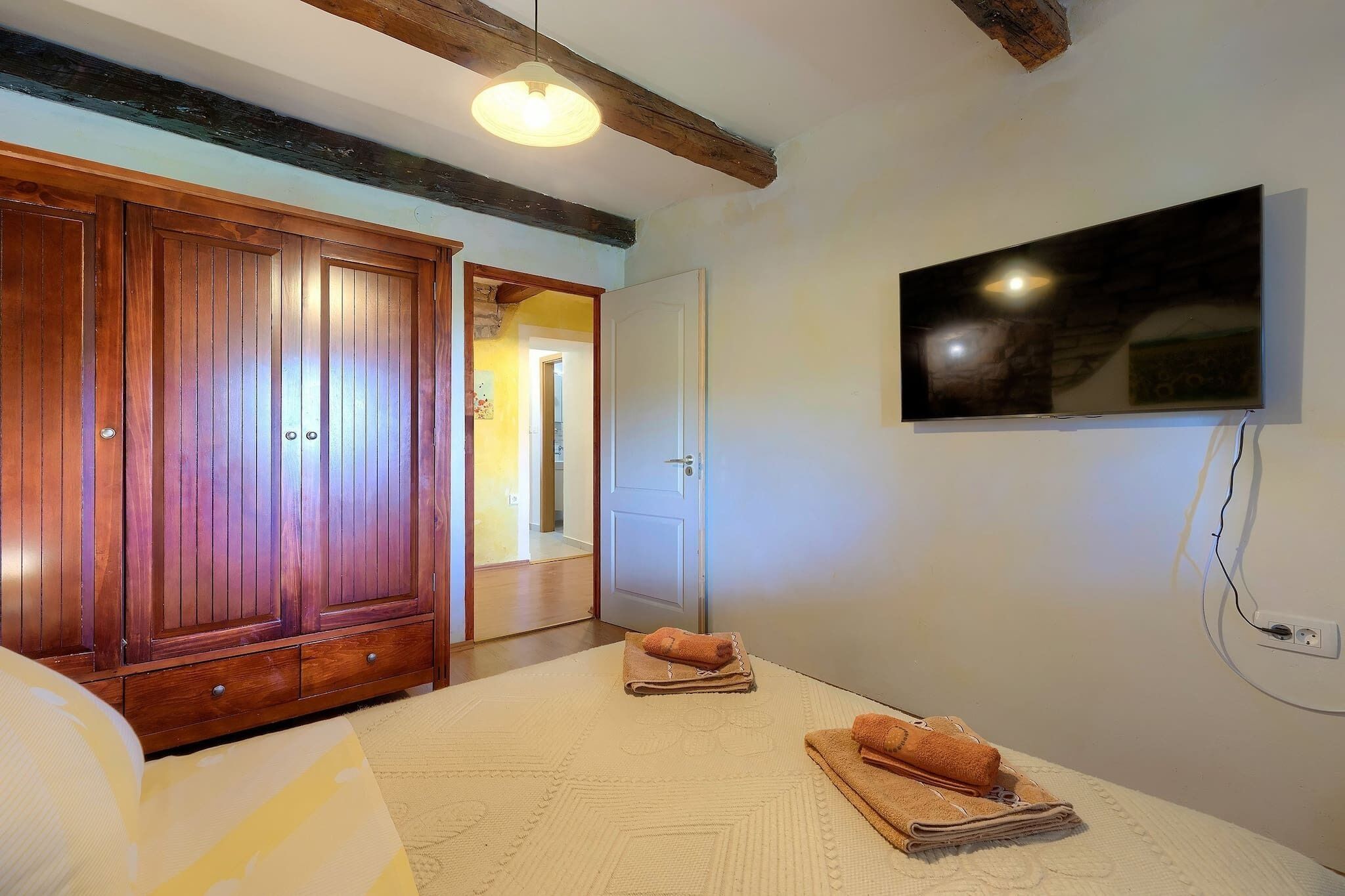 Une chambre dotée d’une grande armoire, d’un téléviseur à écran plat fixé au mur et d’un lit recouvert d’une couvre-lit à motifs blancs et jaunes.