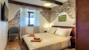 A bedroom with a stone wall, a bed with pillows, a chair, and a TV. - Wonderful Villa Prisedi with Private Pool (Rakalj)