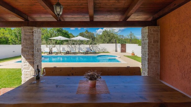 A wooden table with a bottle and glass, overlooking a swimming pool with lounge chairs and umbrellas. - Wonderful Villa Prisedi with Private Pool (Rakalj)