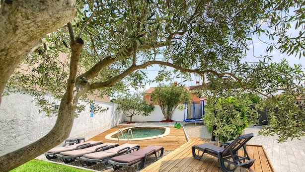 Un patio trasero con una terraza de madera, sillas de descanso, una piscina pequeña y un árbol.