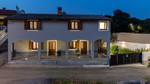 Una casa de dos pisos con techo de tejas, chimenea y balcón con barandilla.