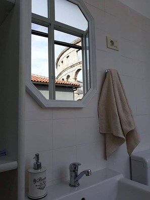 A bathroom with a window, a towel rack, a sink, and a soap dispenser.