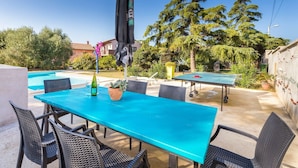 Une terrasse extérieure avec une table et des chaises bleues, une piscine et une table de ping-pong.