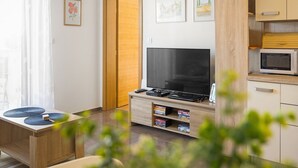 A modern living room with a flat-screen TV, wooden furniture, and a kitchen area with a microwave. - Cute City Apt with a Relaxing Terrace - Tania (Pula)
