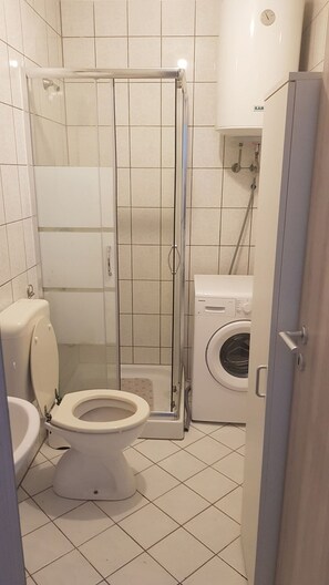 Een badkamer met een toilet, een douchecabine en een wasmachine.