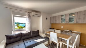 A modern living room with a grey sofa and a dining area with a wooden table and white chairs. A window with a view of the sea is visible. - Lovely Sea View Apartment - Belvi C1 (Medulin)