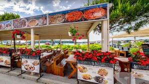 An outdoor restaurant with wooden tables and benches, surrounded by greenery and a view of the sea. - 150 m from the Beach, Medulin Center - Belvi C2 (Medulin)