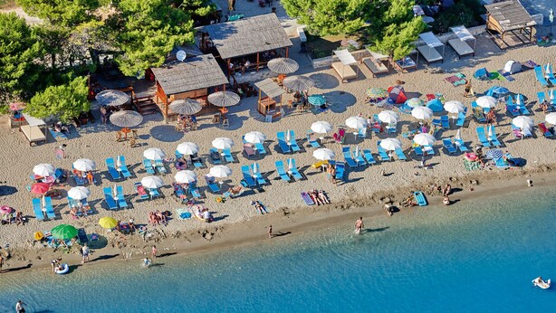 An aerial view of a beach with numerous sun umbrellas, lounge chairs, and a small wooden structure. - 150 m from the Beach, Medulin Center - Belvi C2 (Medulin)