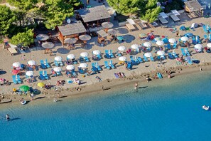 Vue aérienne d’une plage avec de nombreux parasols, des chaises longues et une petite structure en bois.