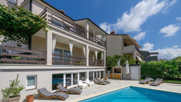 Un bâtiment moderne à deux étages doté d’une piscine, de chaises longues et d’un espace extérieur couvert.