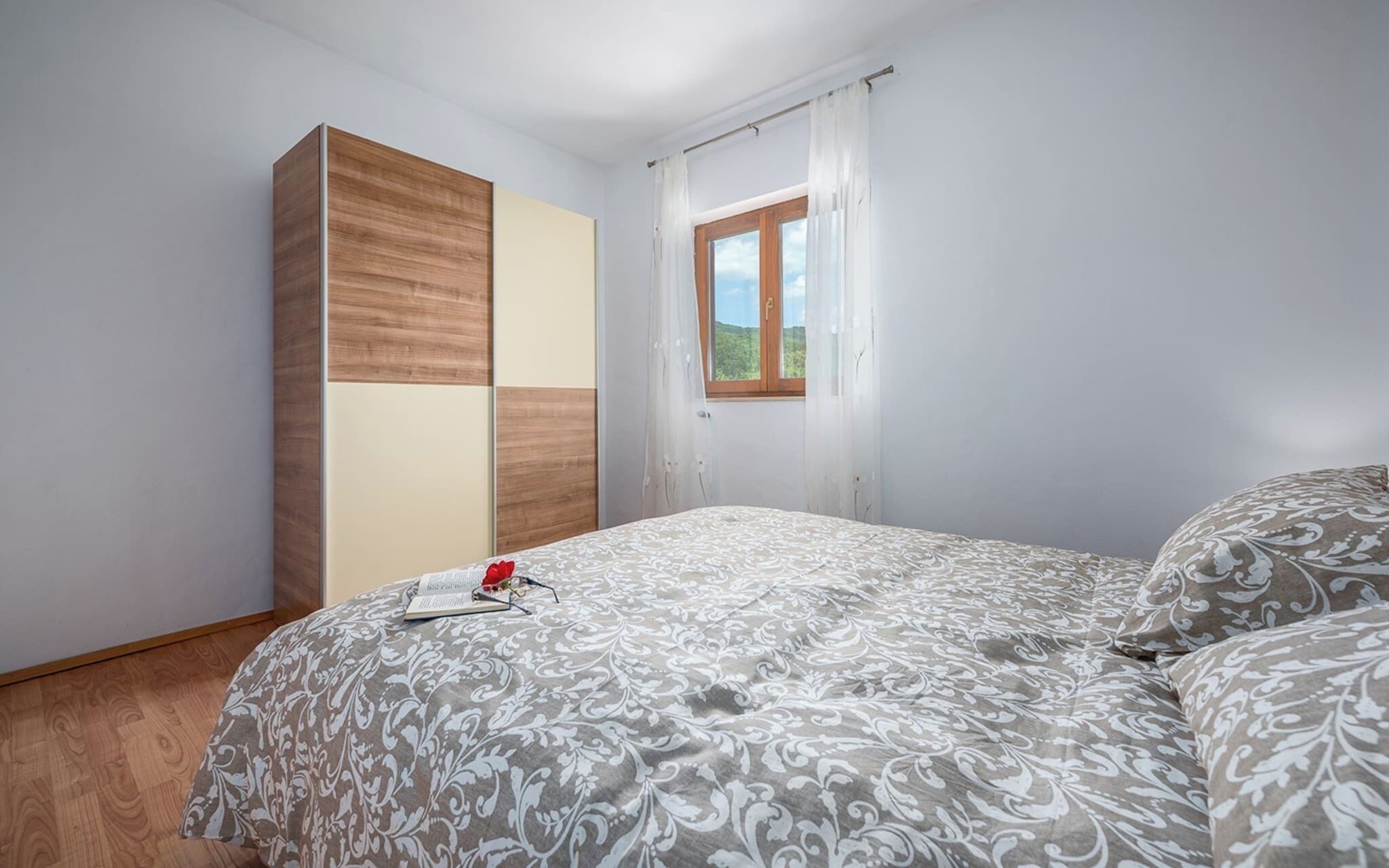 A bedroom with a bed, a wardrobe, and a window with curtains.